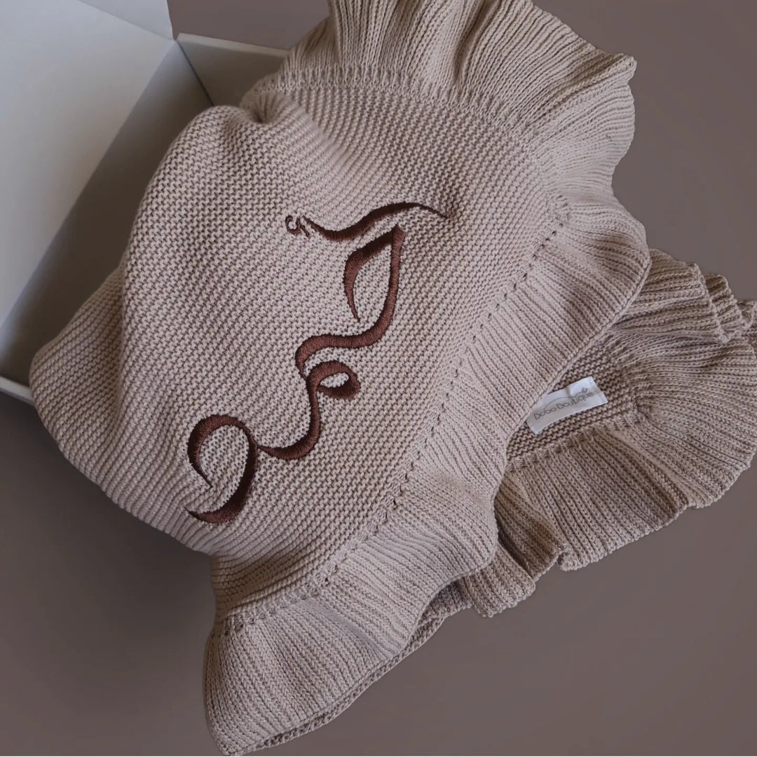 A ruffled hat with a brown decorative swirl design on top, set against a neutral backdrop, perfectly complements the soft Ruffled Blanket by BOBO BOUTIQUE.